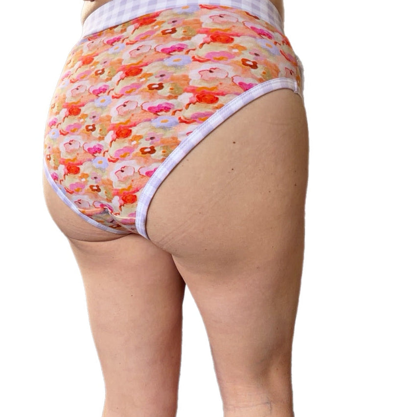 Rear view of a person wearing floral patterned underwear with a white and lavender gingham waistband, shown against a plain white background.