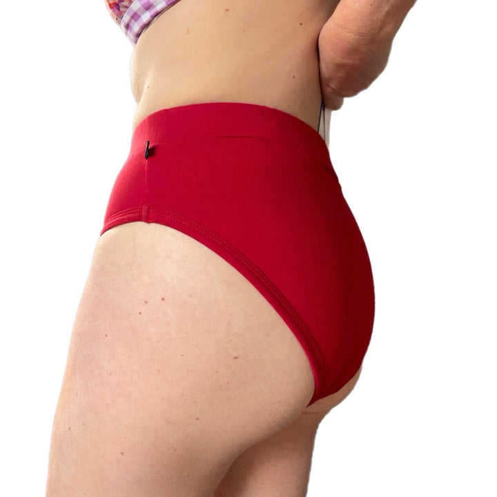 A close-up side view of a person wearing bright red high-waisted bikini-style bottoms against a plain white background.