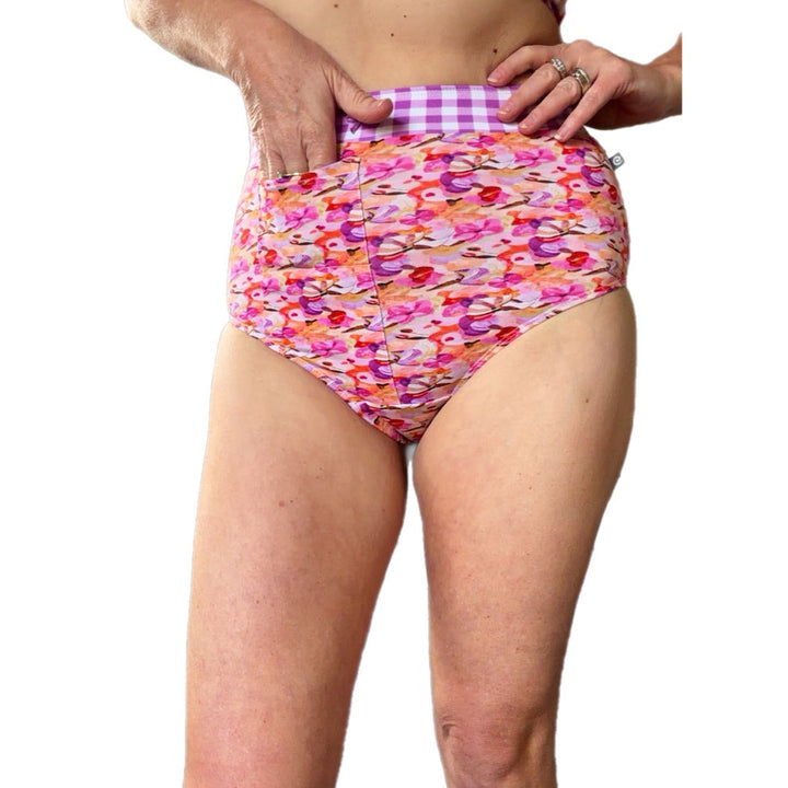 A person wearing high-waisted bikini bottoms with a colorful floral pattern and a purple-and-white gingham waistband, shown against a plain white background.