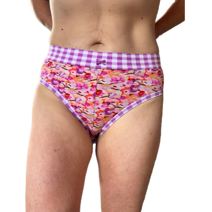 A model wearing high-waisted bikini bottoms with a purple and white gingham waistband and a colorful floral print body, shown against a plain white background.