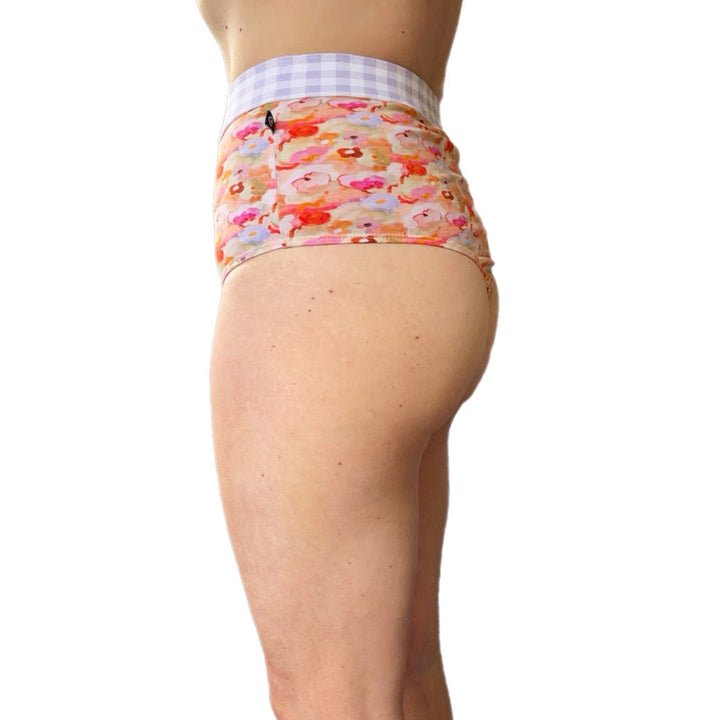 Rear view of a person wearing high-waisted underwear with a colorful cartoon pattern and a light purple-and-white gingham waistband, shown against a plain white background.