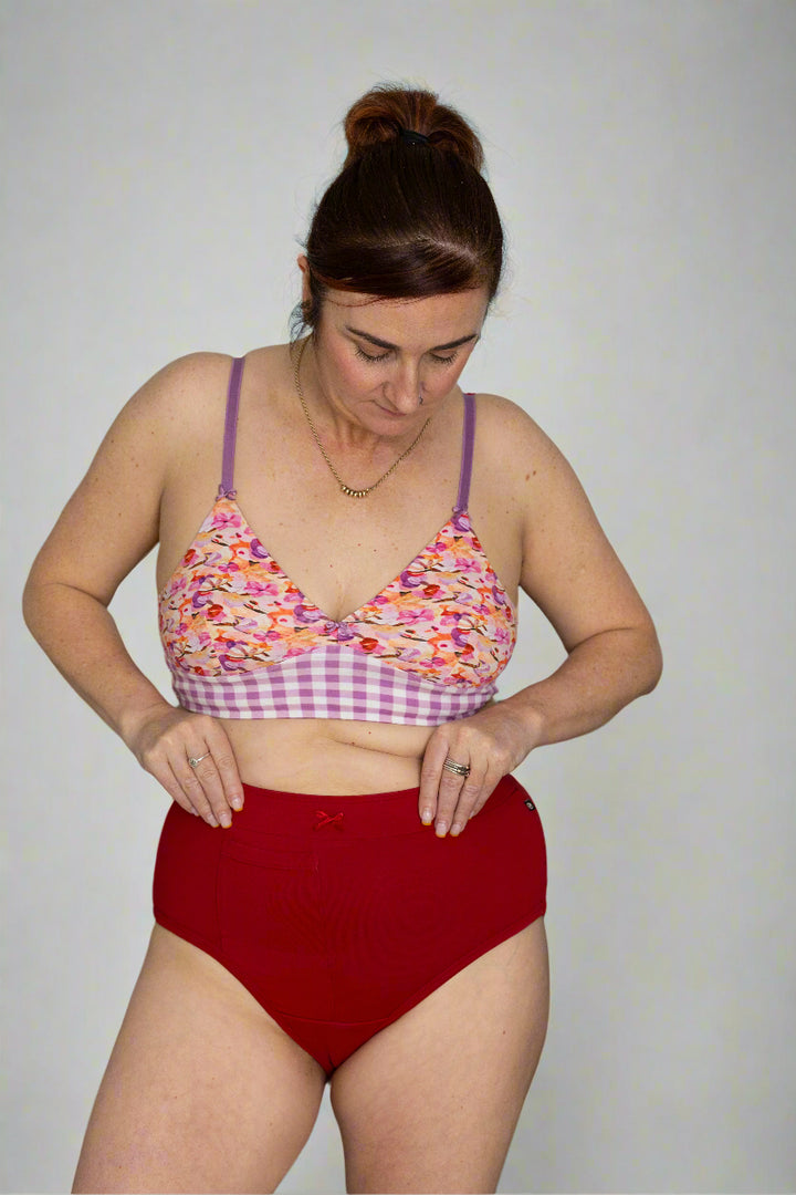 Woman with brown hair wearing floral bralette and red discharge friendly underwear.