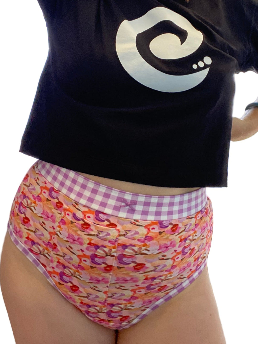 Person wearing a black t-shirt with a logo and colorful patterned underwear indoors.
