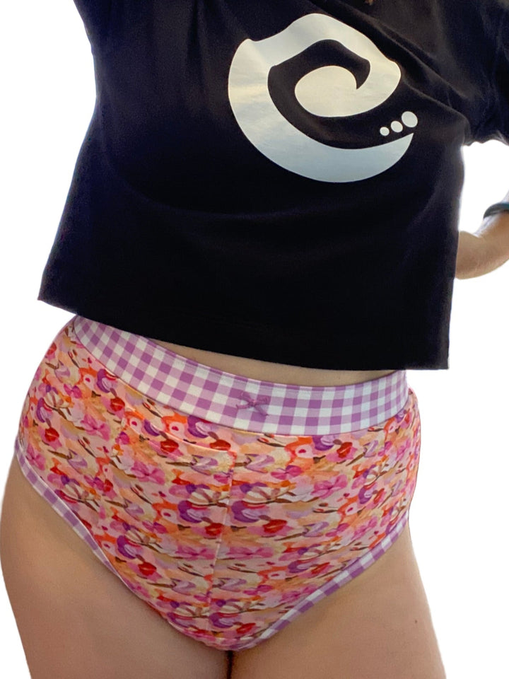 Person wearing a black t-shirt with a logo and colorful patterned underwear indoors.
