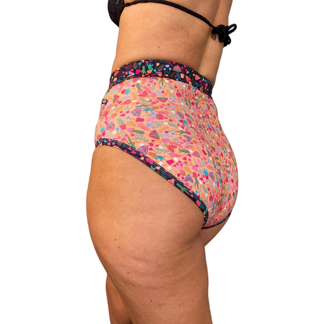A woman wearing high-waisted discharge underwear that has black and coral coloured fabric with butterflies and plants.